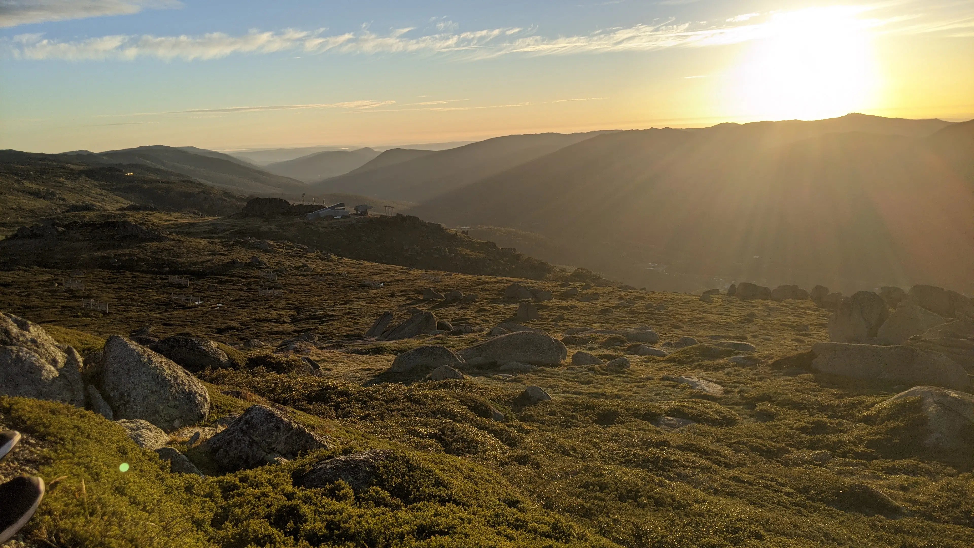 Sunset over a mountainous landscape with rocky terrain and grass.