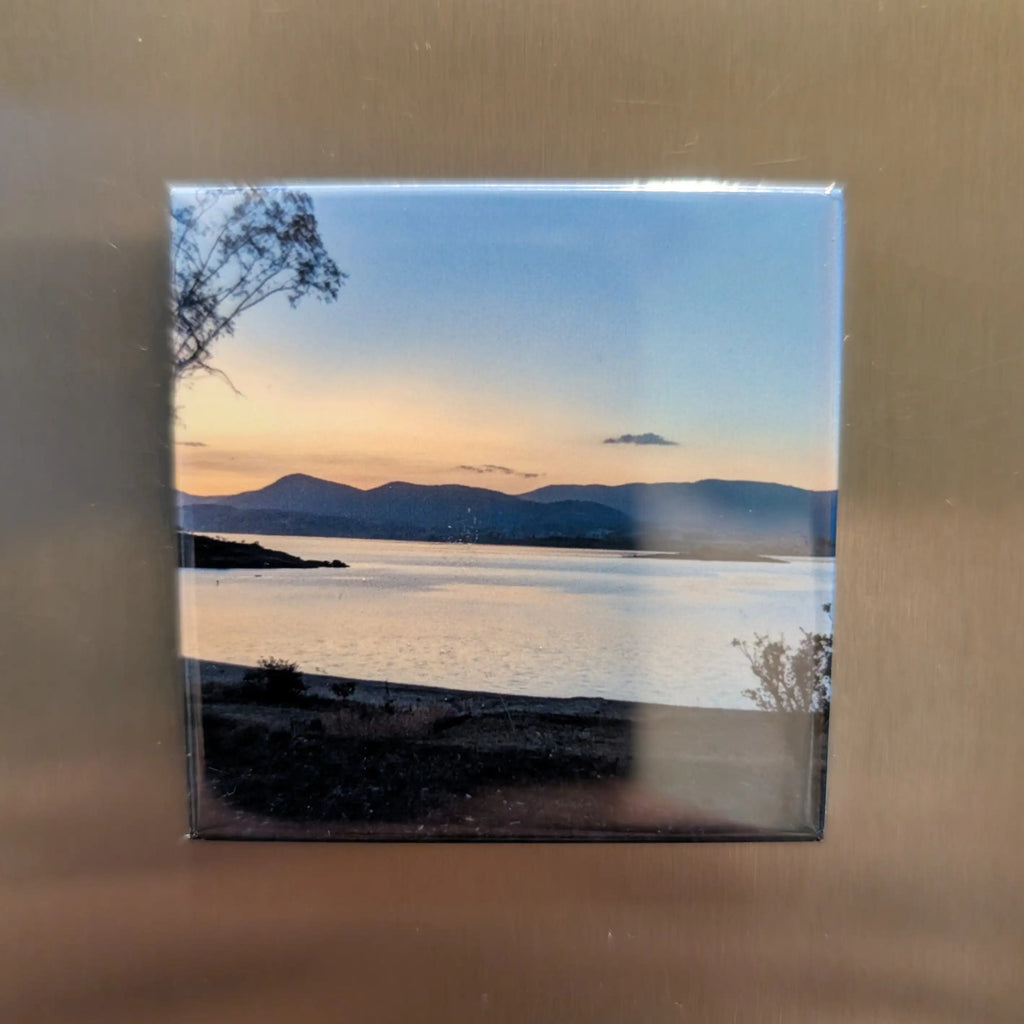 Framed photograph of a sunset over water with mountains in the background, mounted on a metallic surface.
