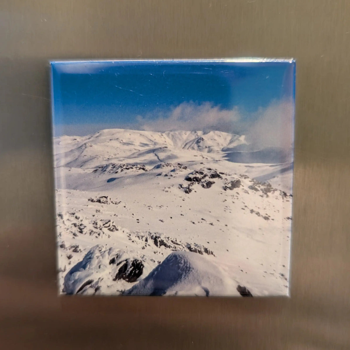 Fridge magnet with a snowy mountain landscape on a metallic surface