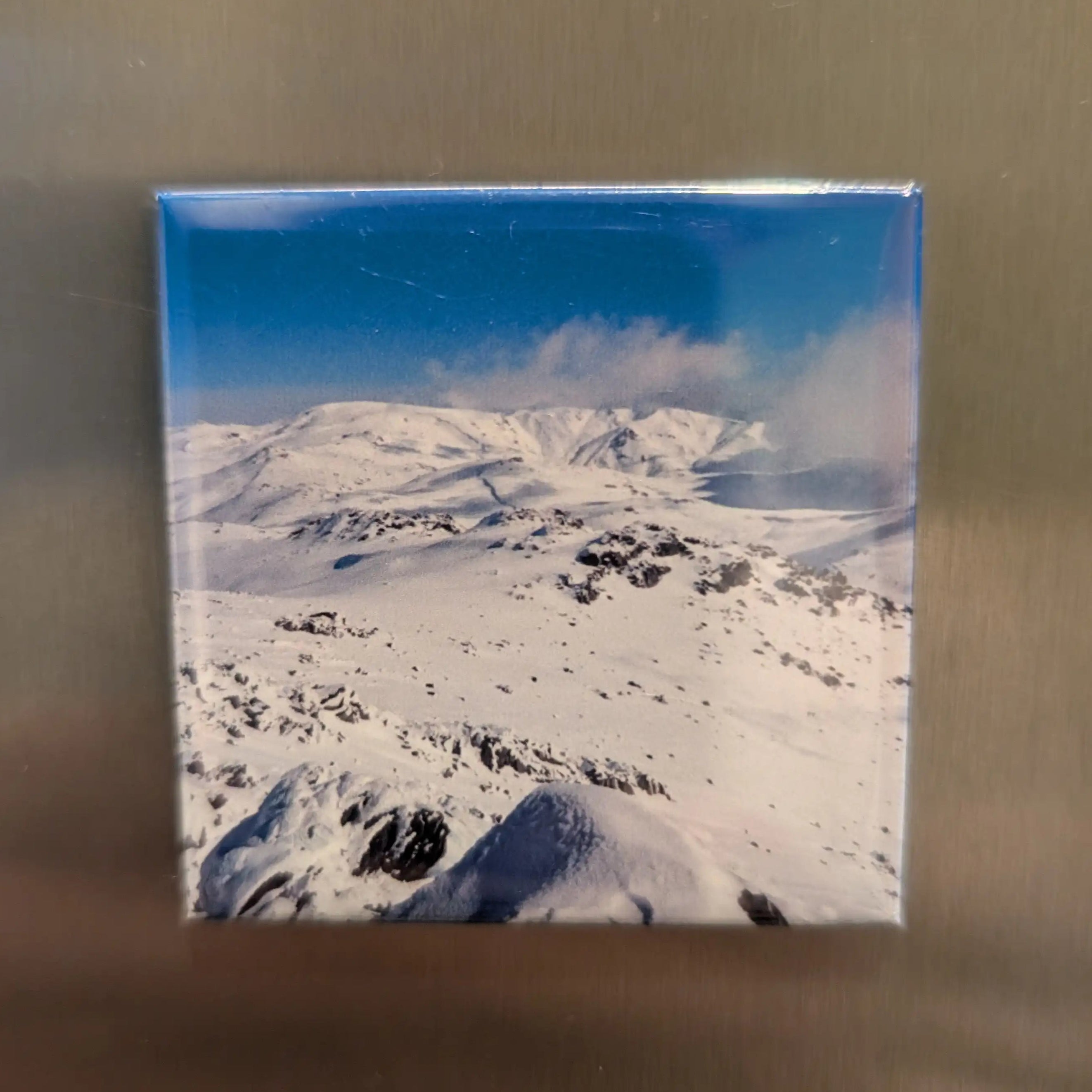 Fridge magnet with a snowy mountain landscape on a metallic surface