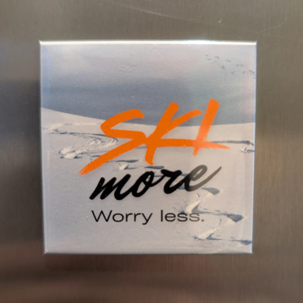 Fridge magnet with 'Ski more, Worry less.' text on a metallic surface