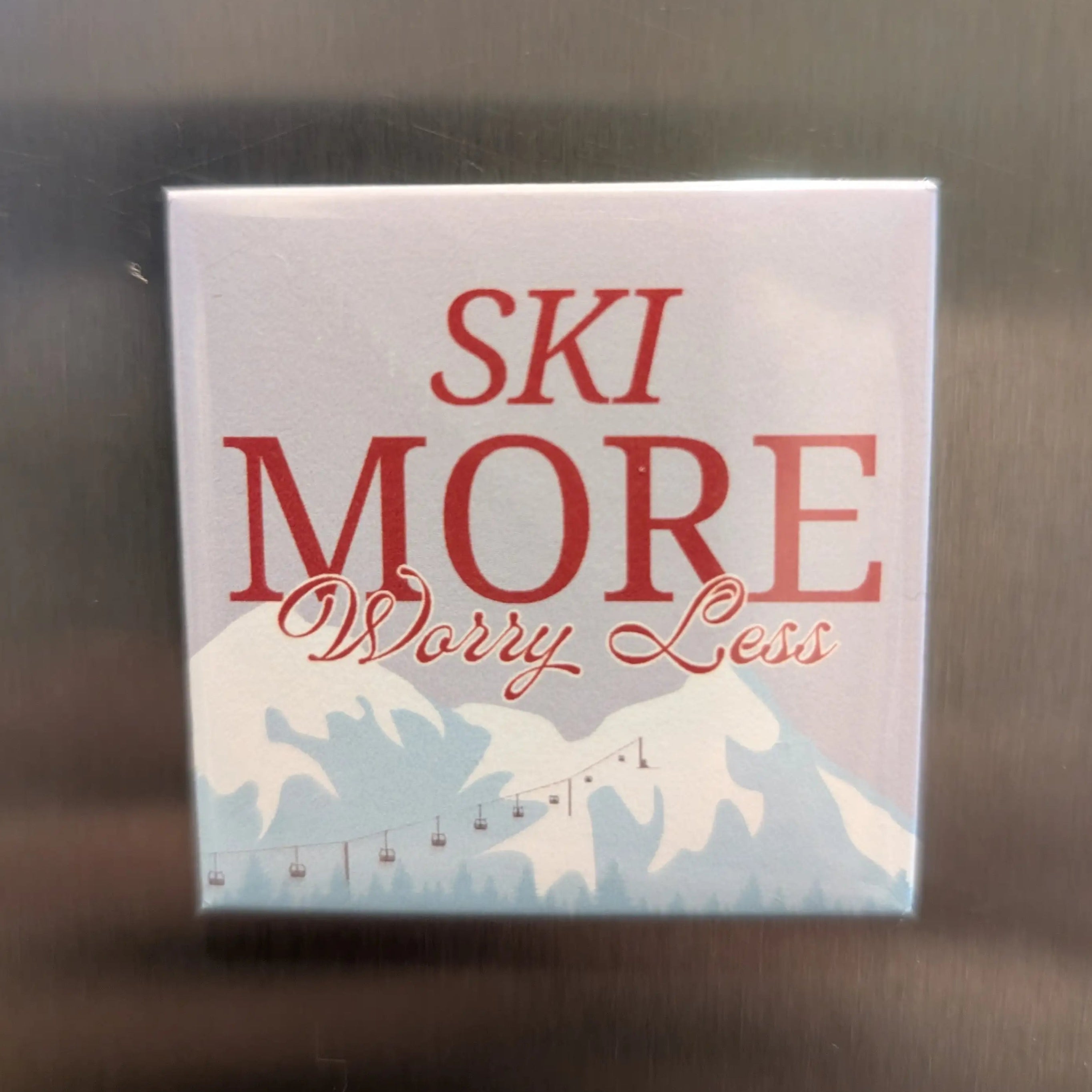Square magnet with 'Ski More Worry Less' text on a reflective surface