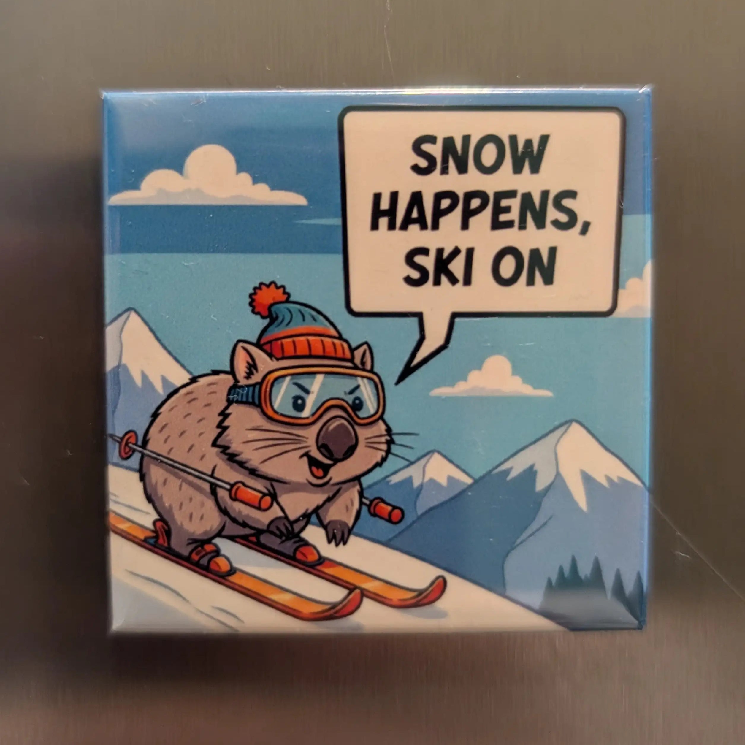 Cartoon wombat on skis with a speech bubble saying 'Snow happens, ski on' against a mountain background.